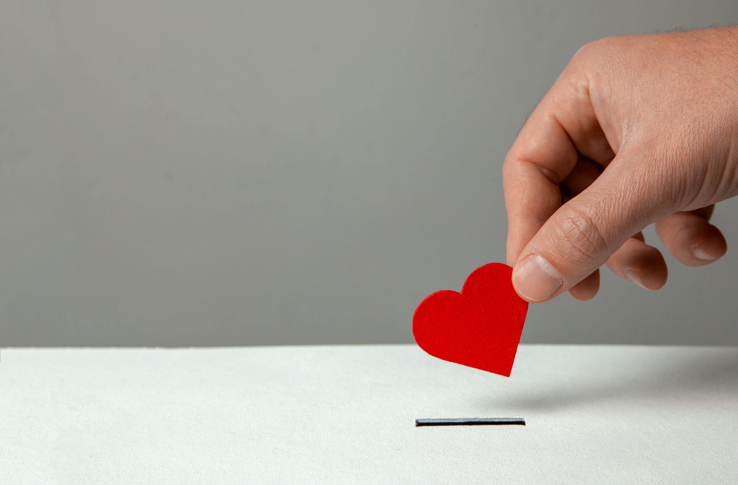 Man’s hand places heart in the donation slot. The concept of t